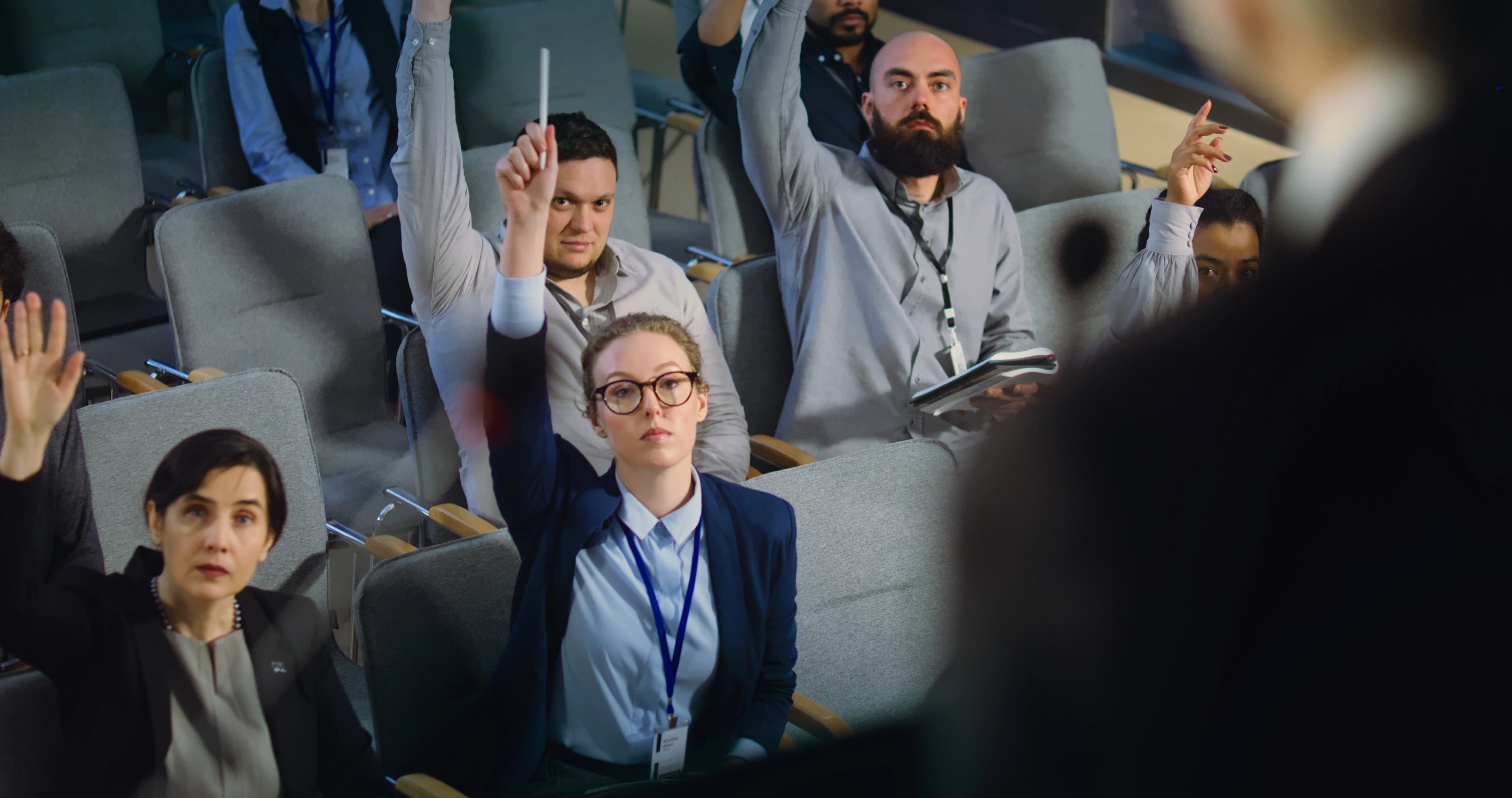 Diverse journalists, media workers raise hands and ask questions during press conference with politician. Press officer or activist gives interview for television in government building hall. Close up