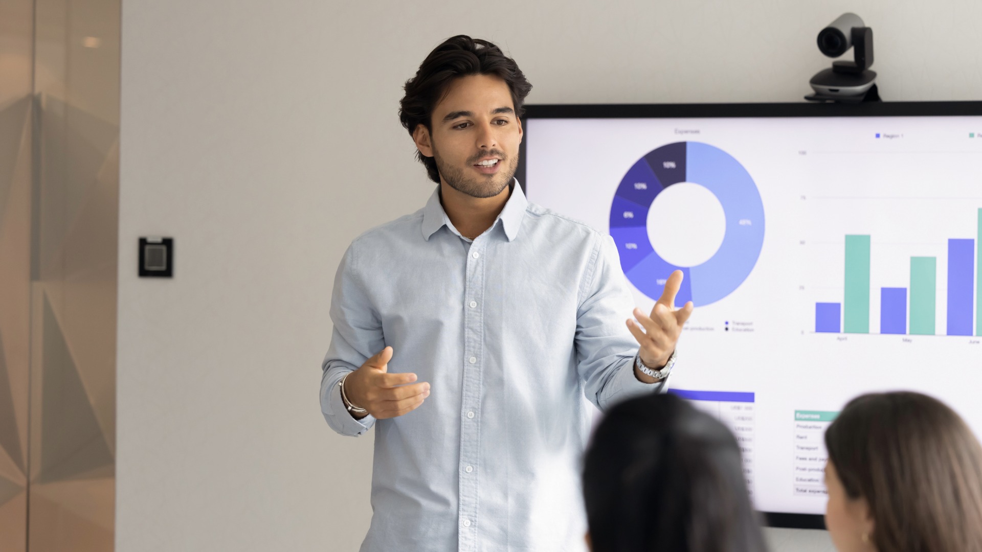 Young business teacher man training new employees, interns, giving marketing seminar. Manager presenting financial sales report to colleagues, standing and speaking at wall display in office