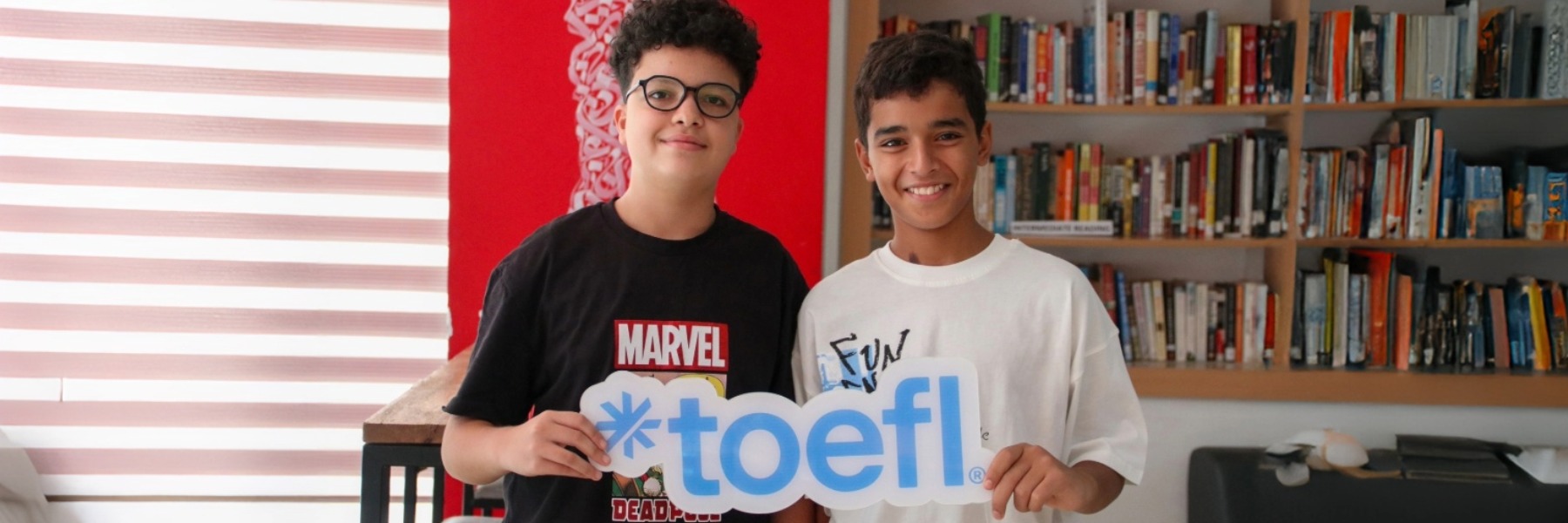 Young student holding a TOEFL logo sign in hands, smiling and ready to take the test in a classroom setting.