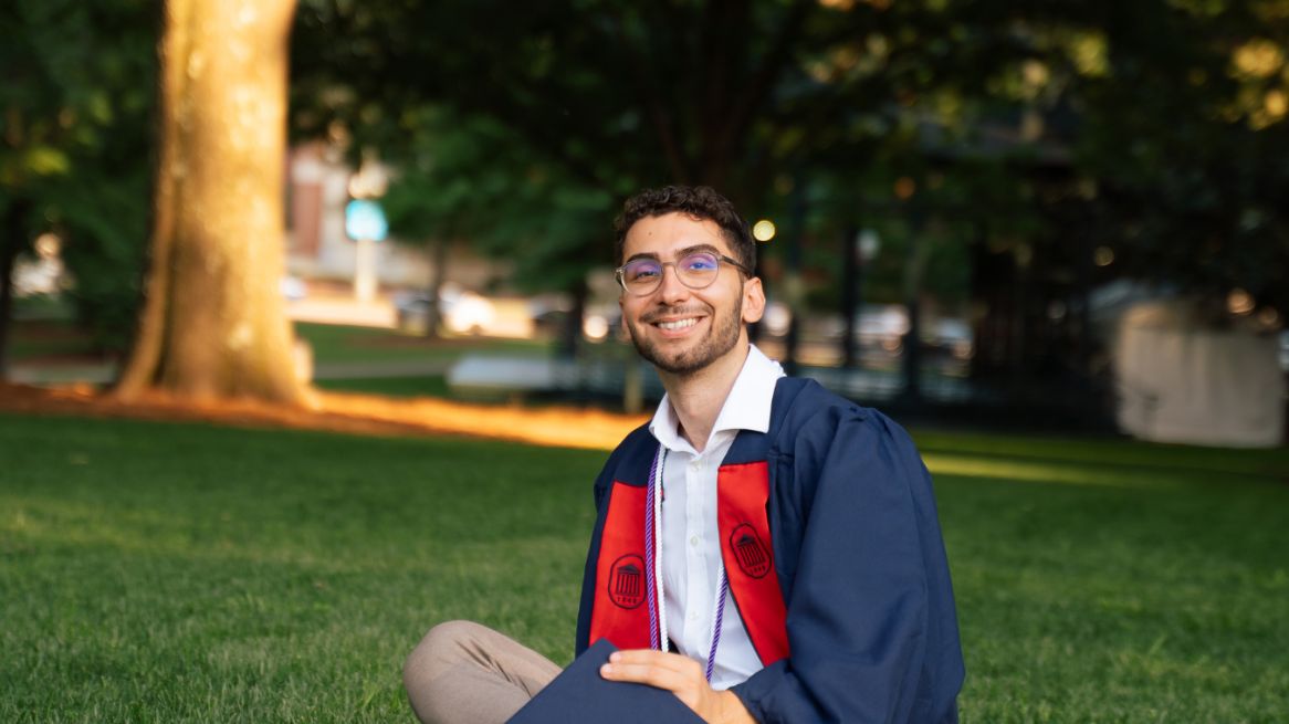 Achref sitting on grass in his graduation gown.