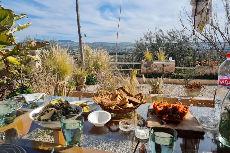 A table is laden with many different dishes. The table is on a balcony overlooking hills in Tunis