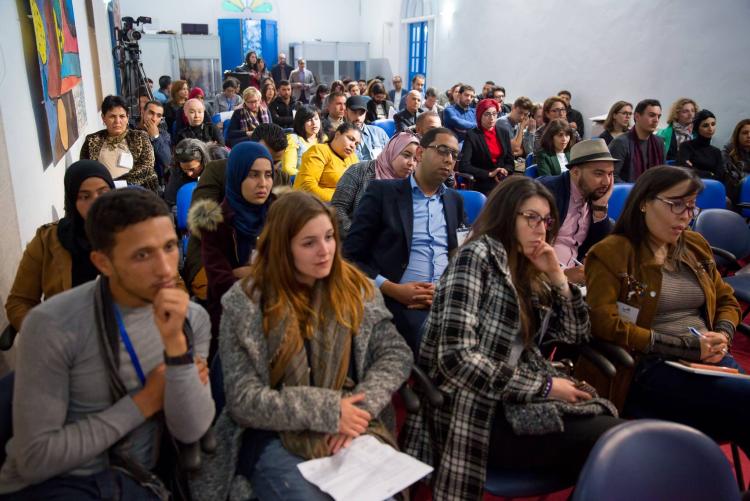 مجموعة كبيرة من الجمهور يجلسون على الكراسي وهم يشاهدون ما هو أمامهم