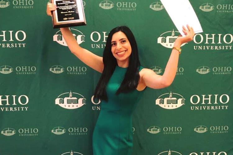 Female student holding up awards in front of Ohio University backdrop