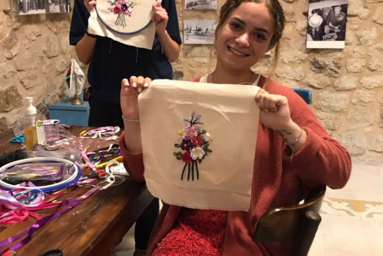 Two women hold up embroidery that they were making with flower patterns