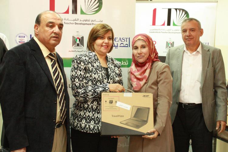 سيدتان تحملان حاسوبًا محمولاً جديدًا أمام يافطة عليها شعار LTD ويقف معهما رجلان
