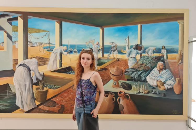 A woman stands in front of a large painting mounted in a museum