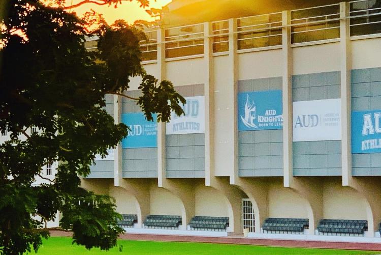 A playing field is in front of the AUD athletics building. The sun is shining over the building and onto the field.