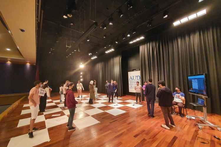 Students play a game of human chess on a stage at AUD