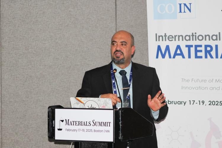 A man is presenting at a Materials Summit. 