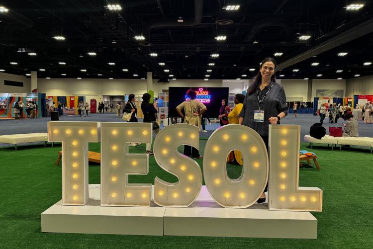 A woman is posing in front of a Tesol sign at a convention event.