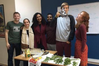 6 students pose in their Arabic classroom during a tea activity. One student is holding up the teapot and the girl beside him is looking up at the teapot. 