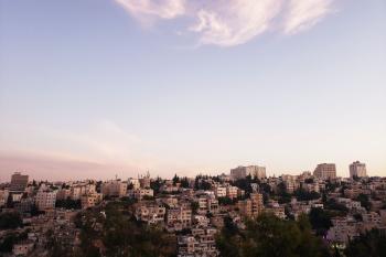 The skyline of Amman at sunset the buildings in the distance and the sky is prominent and a rosy color at the horizon but clear blue at the top.