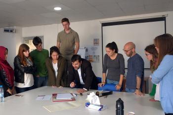 Students stand around their calligraphy teacher who is showing them how to write