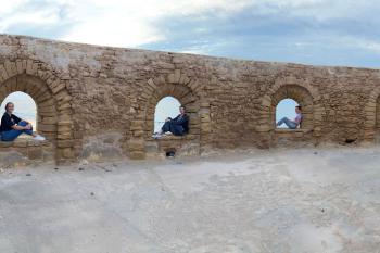 Students sit inside separate arches in a panorama image of an old wall.
