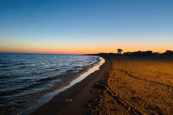 The sun sets over the beach that is on the left of the frame and the sand is on the right and there are no people