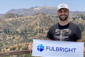 College student in front of Hollywood sign in Los Angeles holding banner with Fulbright program logo