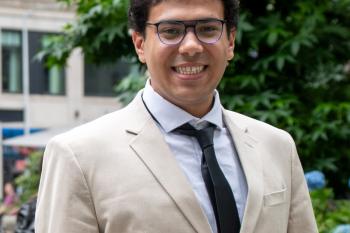 Headshot of Ahmed in a beige blazer and a navy tie