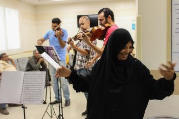 A trio of musician is playing instruments in a hospital. A woman is dancing in the foreground