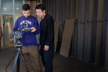Two men next to a camera tripod.