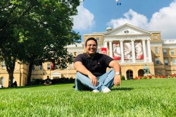 Student standing on lawn in campus in front of buildings 